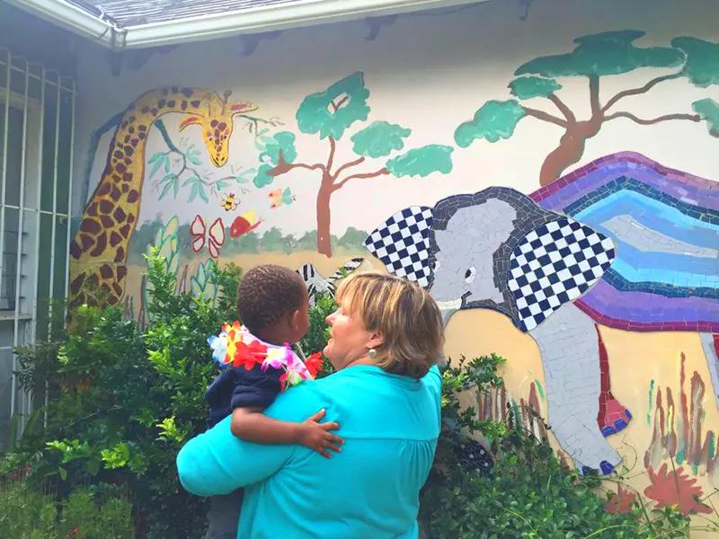 Adopting a baby in Indiana – a picture of a woman holding her small toddler looking at a colorful mural of a giraffe, elephant, and insects. Adoption of Indiana can help dreams like this come true