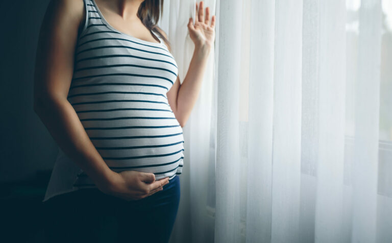 Pregnant woman wearing a black and white striped shirt standing near a window.
