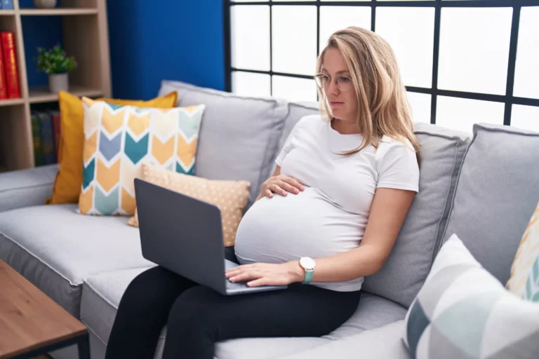 Birthmothers in Adoption: Connecting through the journey. A young pregnant woman using a laptop on the couch, exploring options and seeking support.